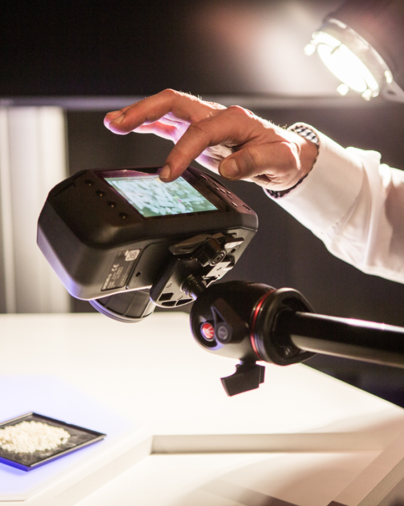 Specim IQ in use attached to a tripod over a sample of rice. Use is navigating data on built-in touchscreen