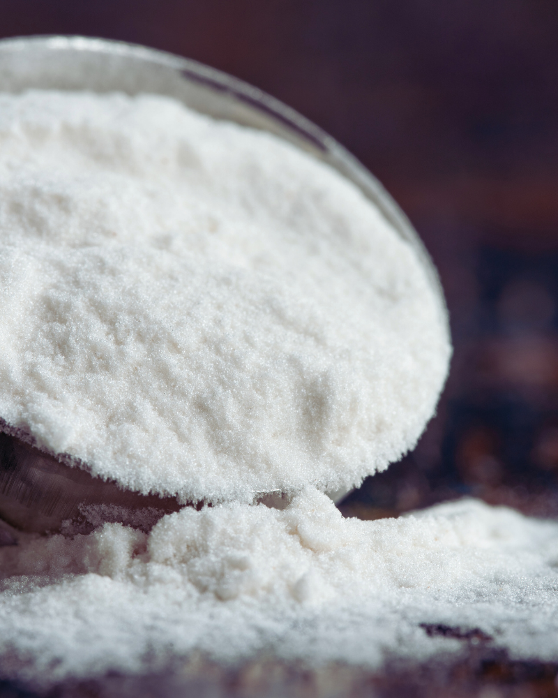 Crystalline white powder in a measuring spoon spilling out onto a surface