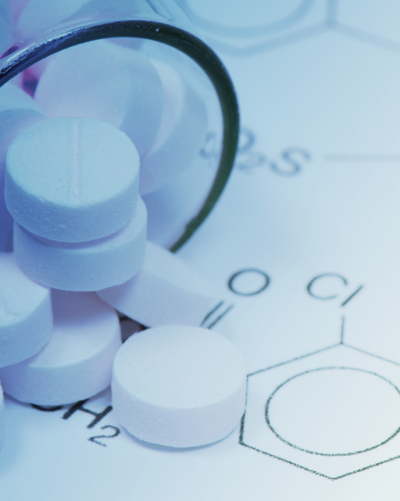 Pill tablets spilling out of a bottle onto a paper with molecular information on it